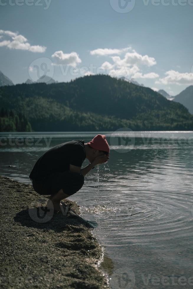 un' uomo lavaggi il suo mani su il riva di un' foresta lago foto