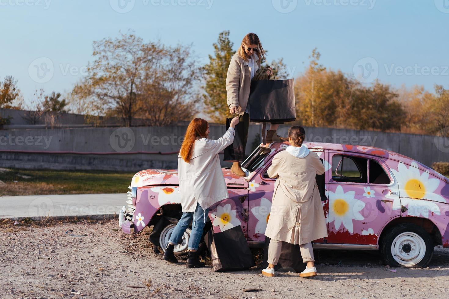 giovane donne in posa vicino un vecchio decorato auto foto