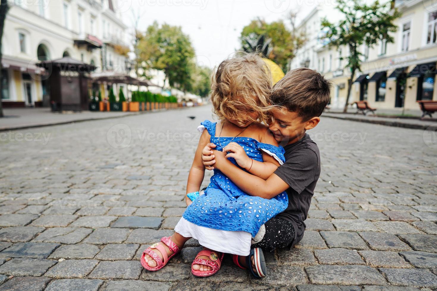 poco ragazzo e ragazza siamo seduta su il strada foto