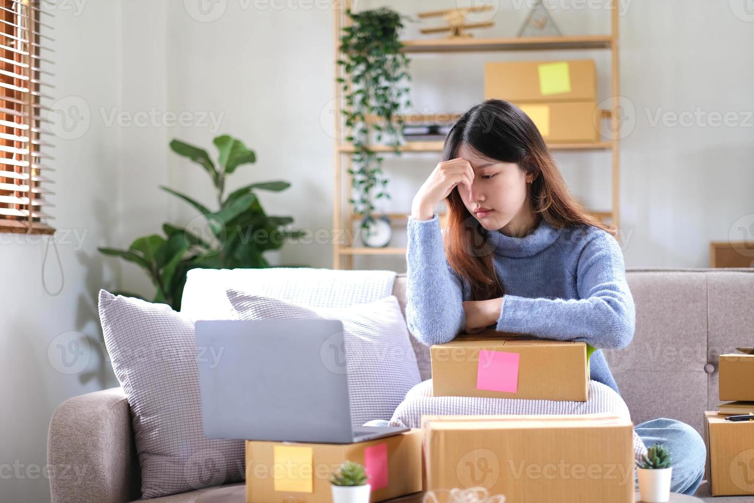 un' giovane asiatico donna Lavorando nel un' piccolo e-commerce attività commerciale è pensiero così stanco e alimentato su con depressione. foto