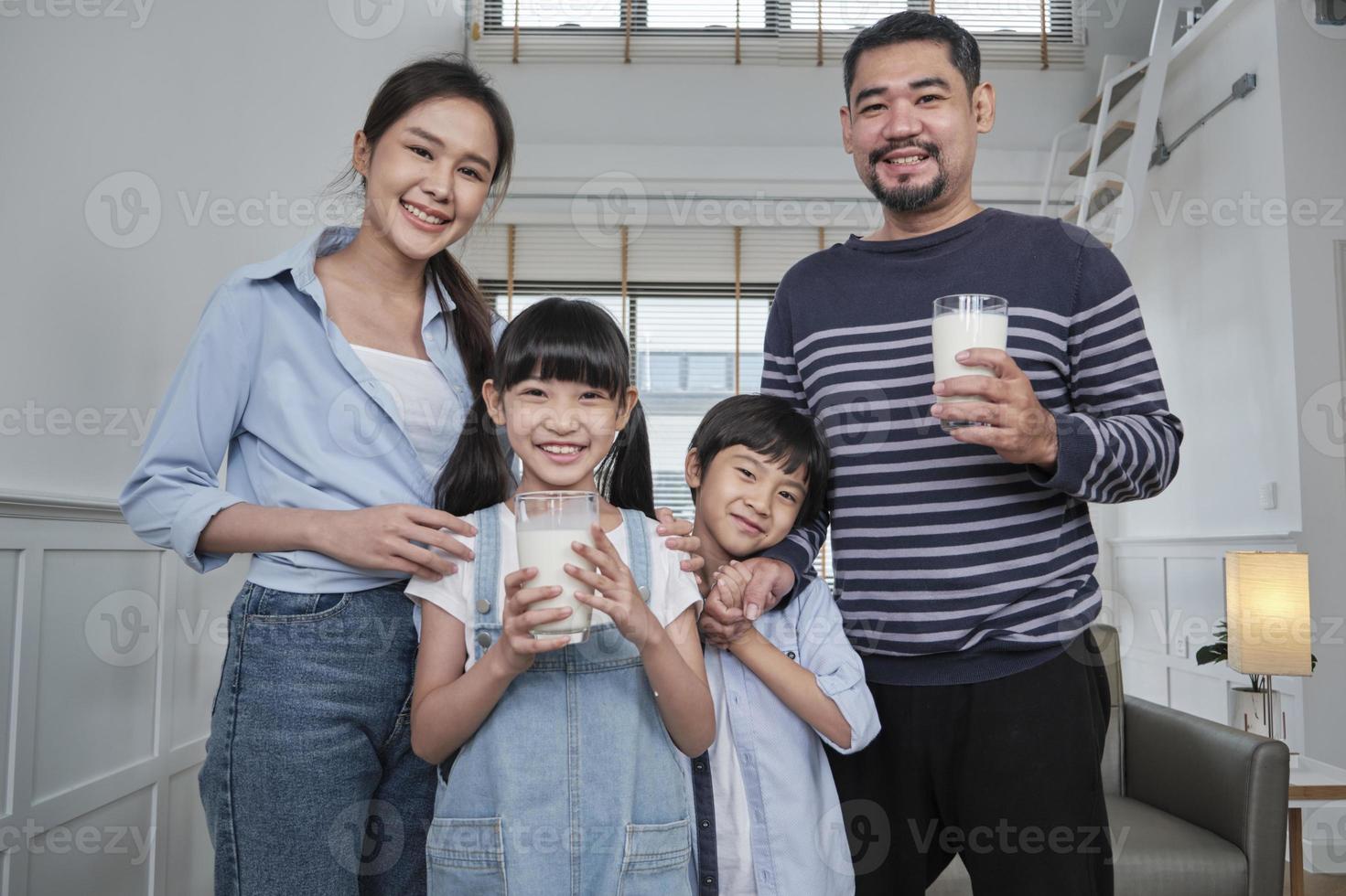 ritratto di contento salutare asiatico tailandese famiglia, poco figli, e giovane genitori con bicchiere di latte nel mattina, Sorridi e Guarda a telecamera insieme a bello casa, benessere nutrizione prima colazione stile di vita. foto