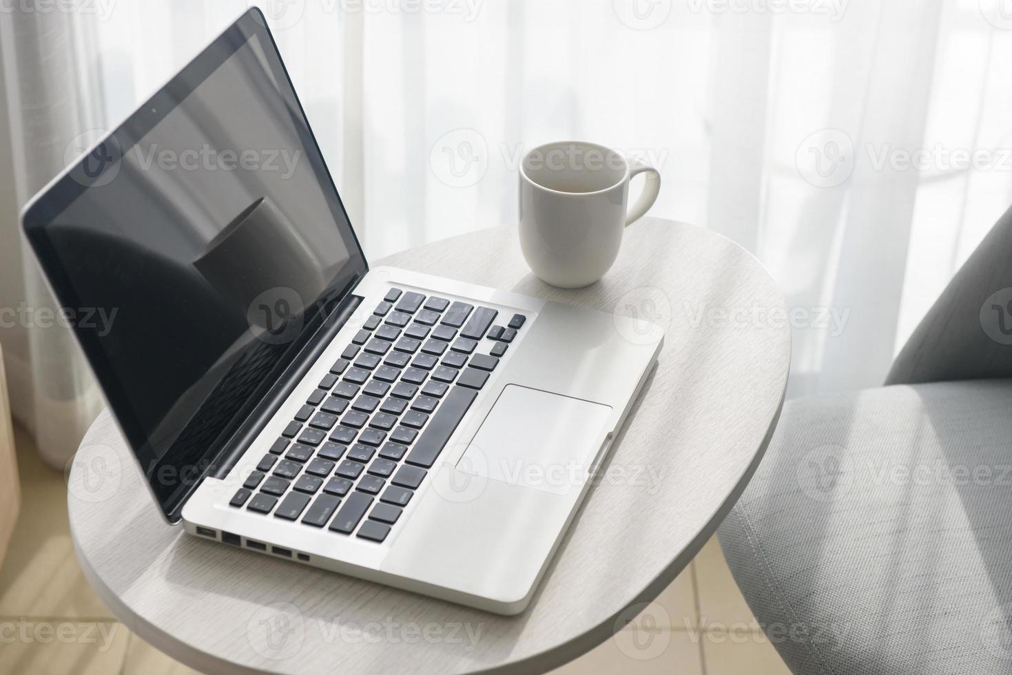 il computer portatile e caffè tazza su tavolo e sedia nel Camera da letto foto