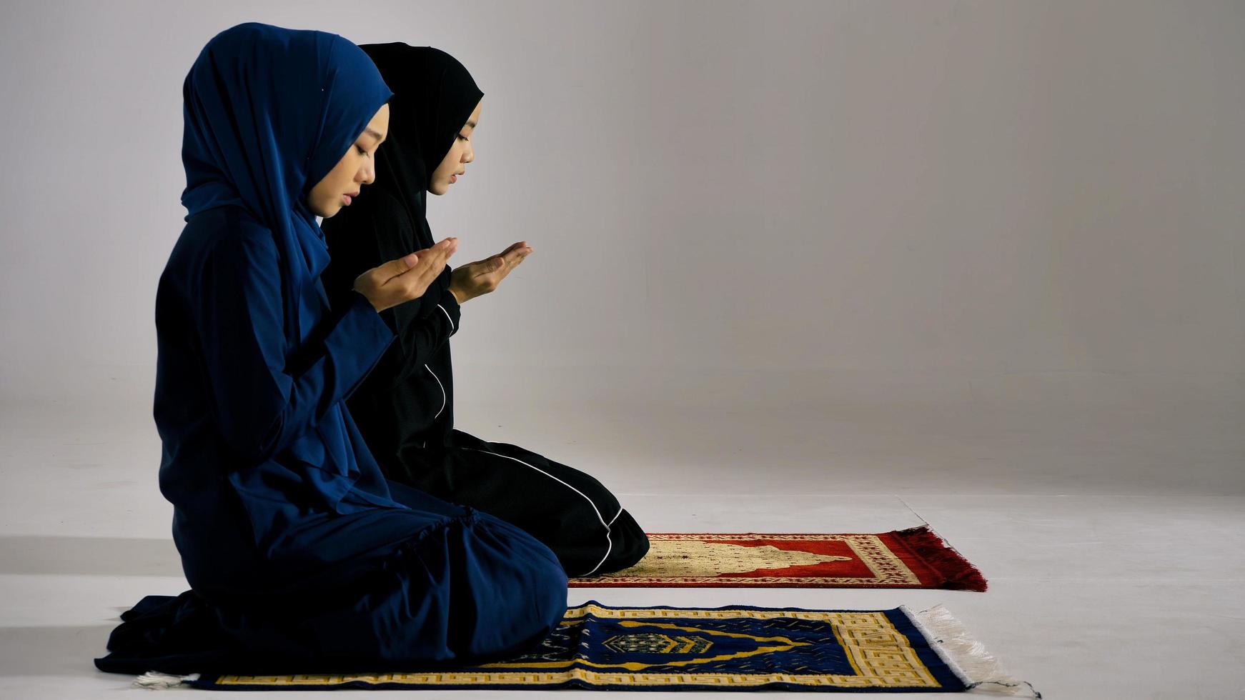 due giovani donne musulmane asiatiche nel tradizionale hijab stanno pregando per glorificare Allah e praticare la fede islamica nella moschea. foto