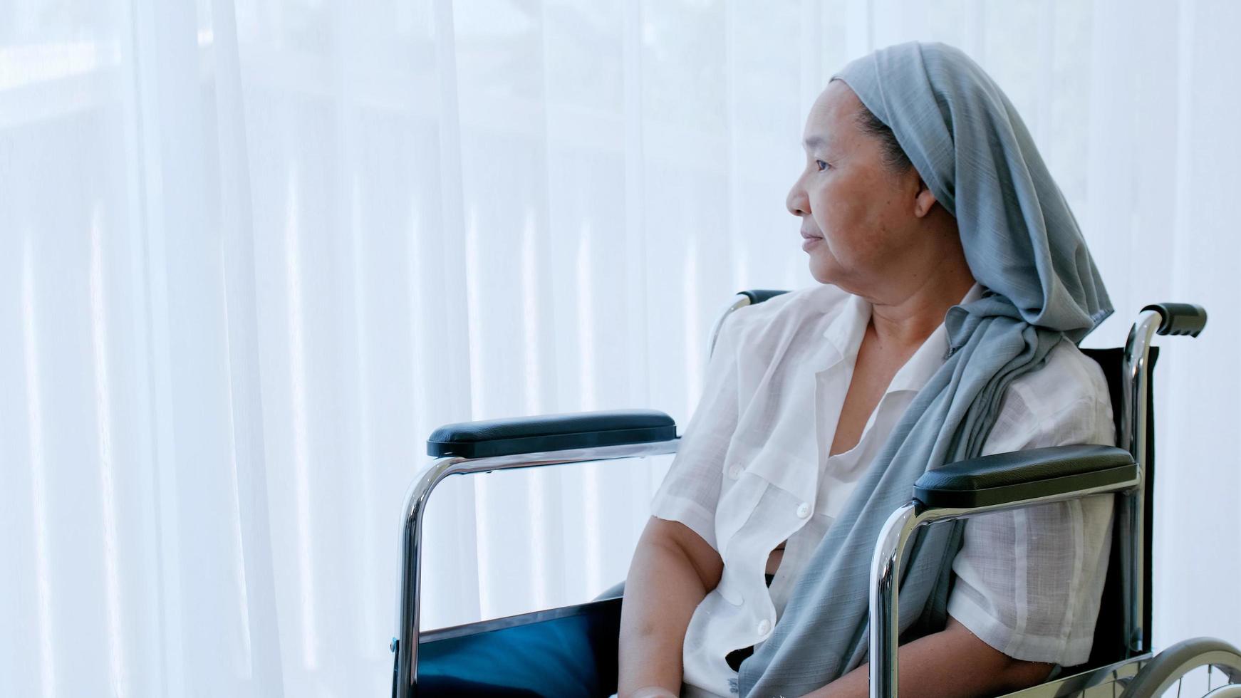 un anziano donna con cancro seduta nel un' sedia a rotelle guardare su di il finestra mentre essere ricoverato in ospedale. foto