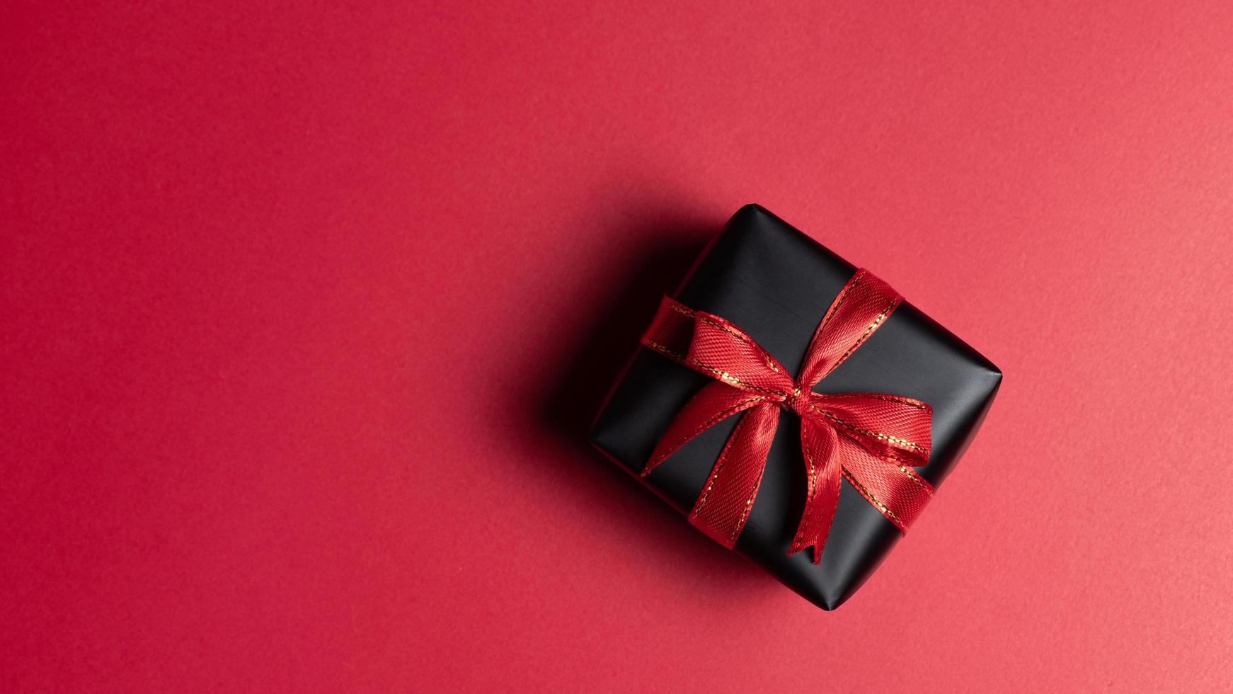 superiore Visualizza di nero regalo scatola con rosso e nero nastri isolato su rosso sfondo. foto