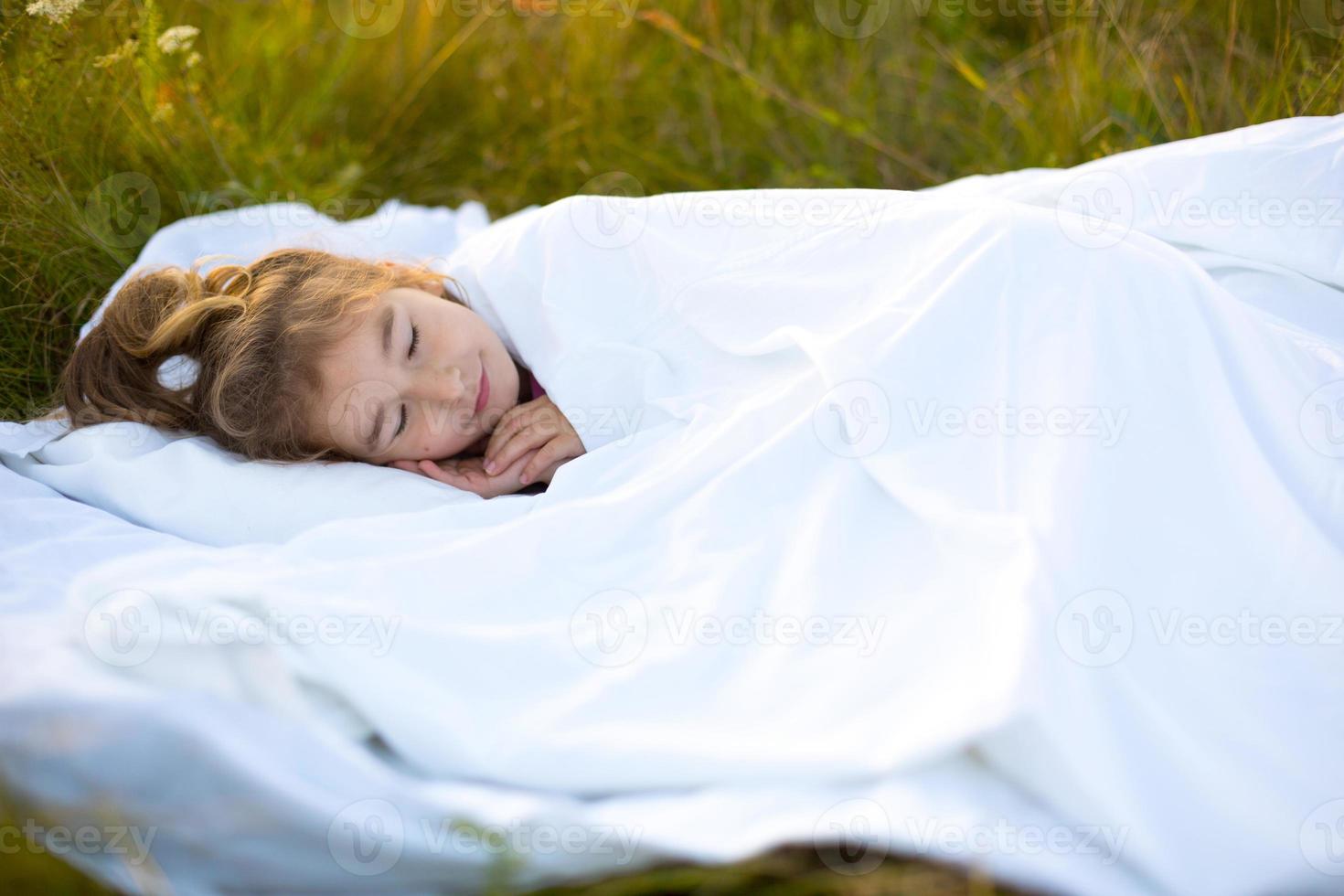 il ragazza dorme su bianca letto biancheria nel natura nel il erba, nel il fresco aria. protezione a partire dal zanzare, salutare dormire, il benefici di ventilazione, indurimento, pulito natura, ecologia, figli di Salute foto