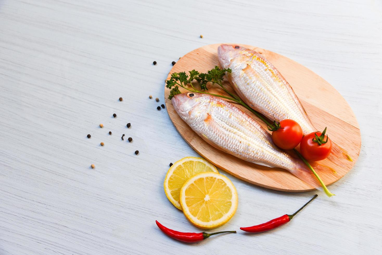 fresco crudo pesce su taglio tavola con pomodoro Limone peperoncino e verde prezzemolo foto