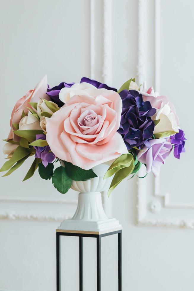 colpo verticale di fiori artificiali su supporto per fiori e vaso alto su sfondo bianco in una spaziosa sala usata come oggetto di decorazione. foto