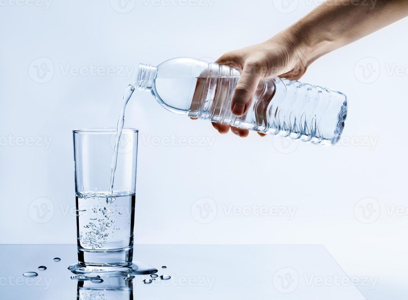mano scrosciante fresco puro acqua a partire dal bottiglia in un' bicchiere su il tavolo con acqua gocce, assistenza sanitaria e bellezza idratazione concetto foto