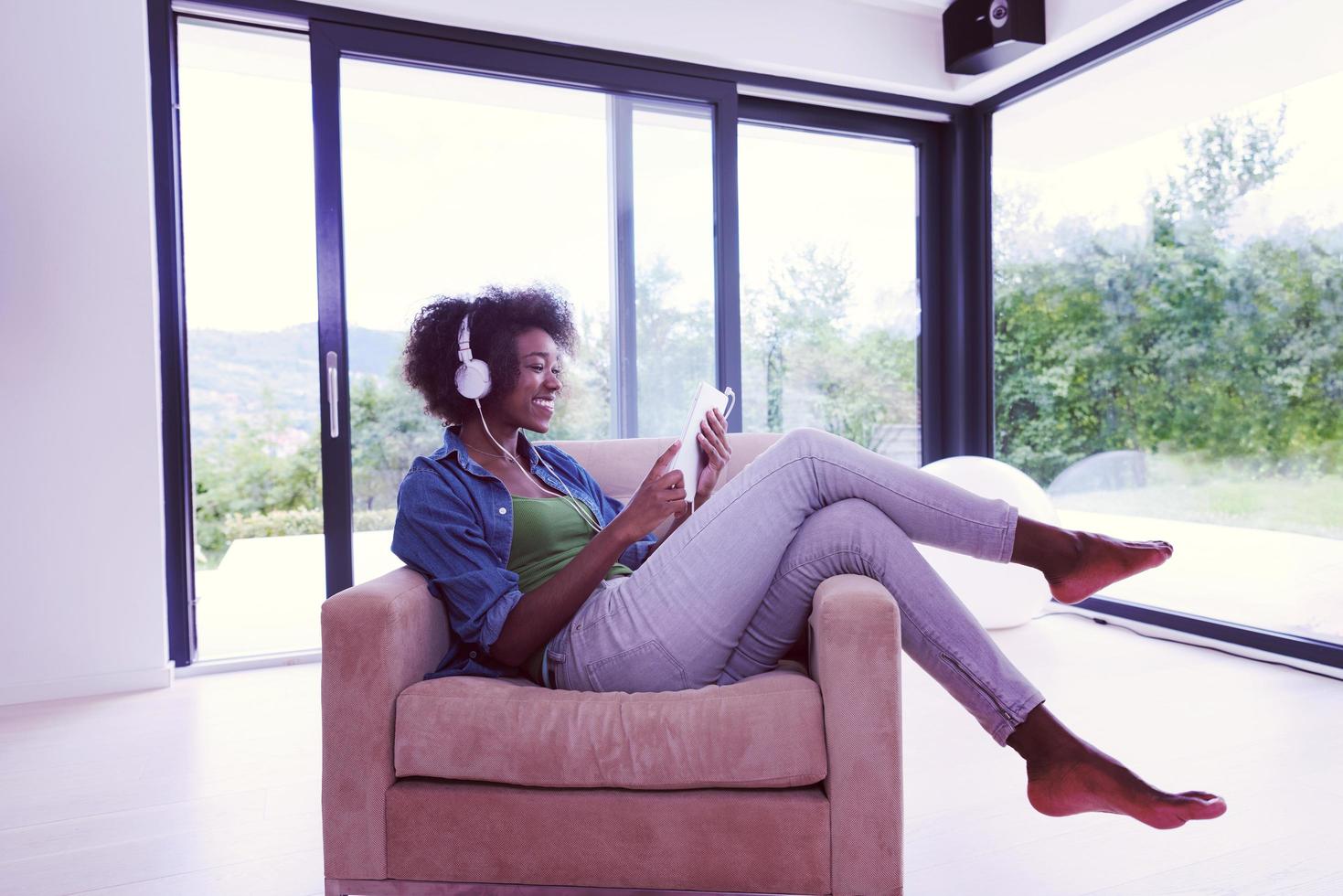 africano americano donna a casa nel sedia con tavoletta e testa telefoni foto