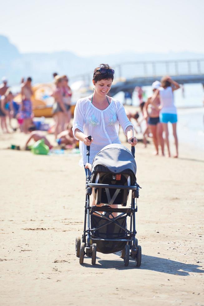 madre a piedi su spiaggia e spingere bambino carrozza foto