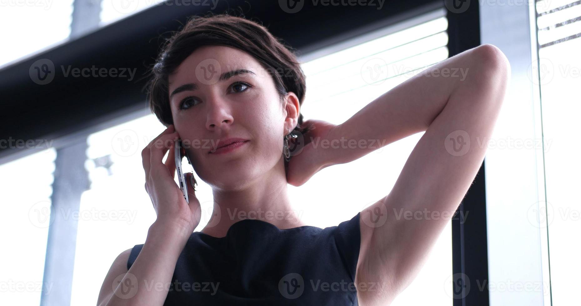 attività commerciale ragazza in piedi nel un' moderno edificio vicino il finestra con Telefono foto