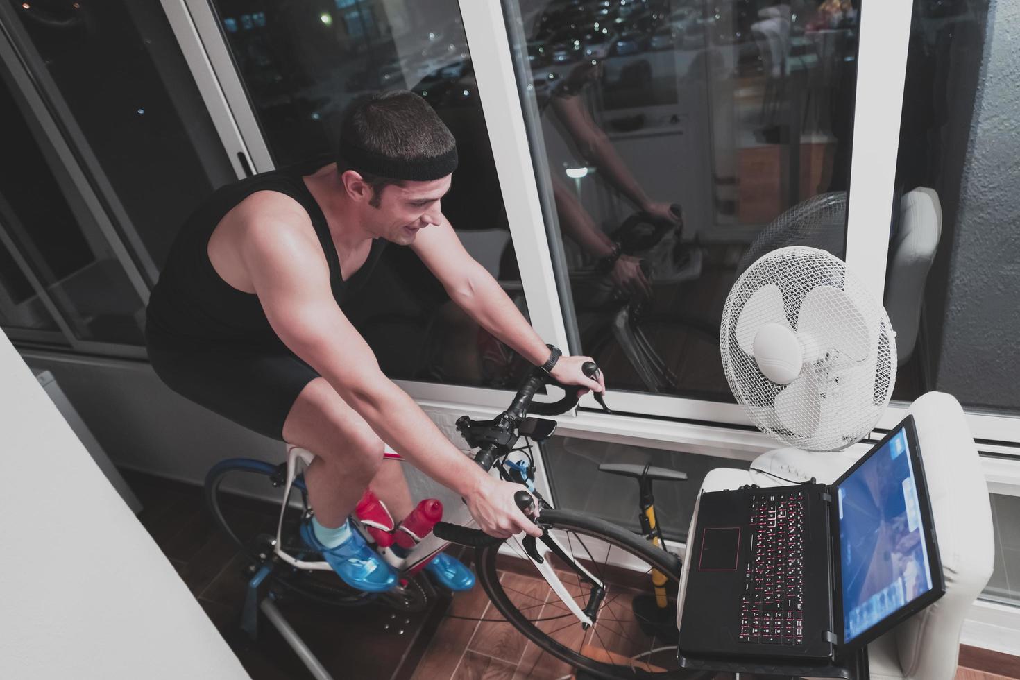 uomo Ciclismo su il macchina allenatore lui è esercizio nel il casa a notte giocando in linea bicicletta da corsa gioco foto