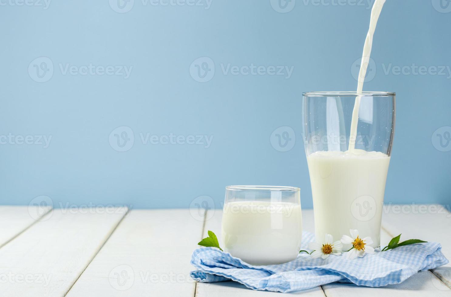 scrosciante un' bicchiere di latte su un' bianca di legno tavolo su un' blu sfondo, gustoso, nutriente e salutare latteria prodotti foto