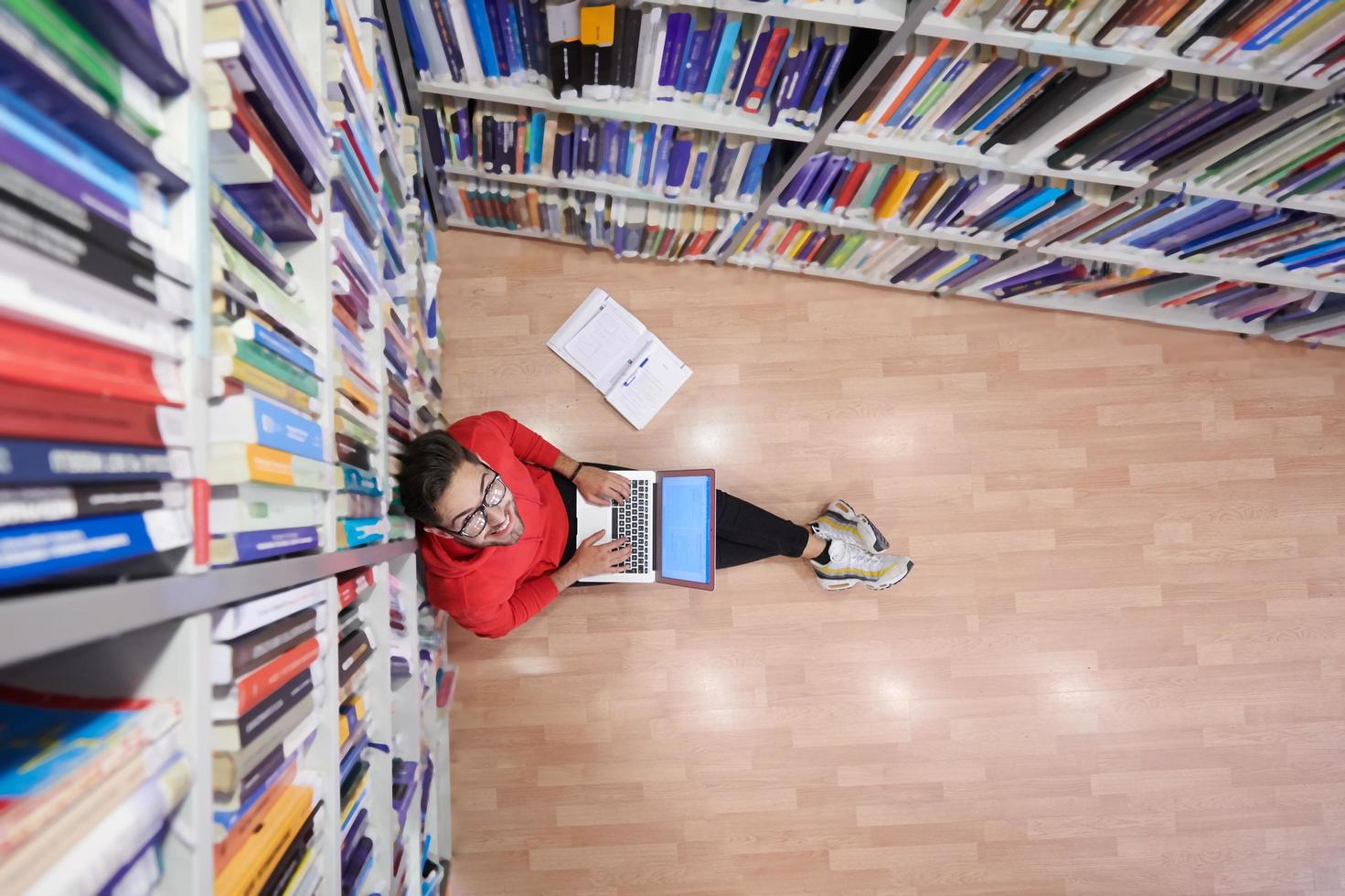 il studenti usi un' taccuino, il computer portatile e un' scuola biblioteca foto