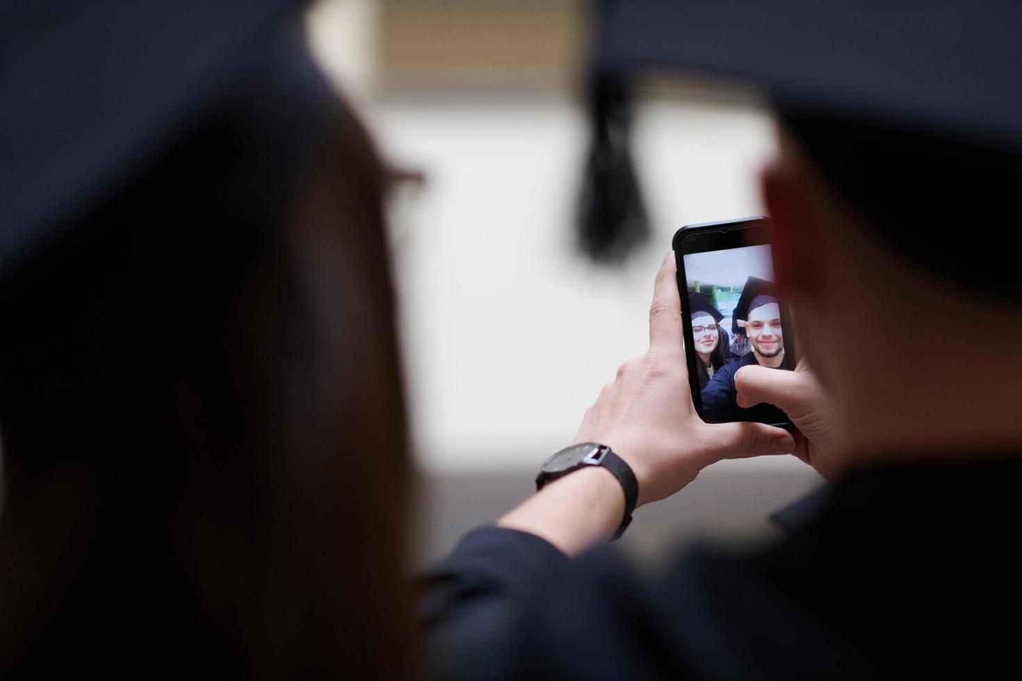 gruppo di contento internazionale studenti nel mortaio tavole e laurea breve abiti con diplomi assunzione autoscatto di smartphone foto