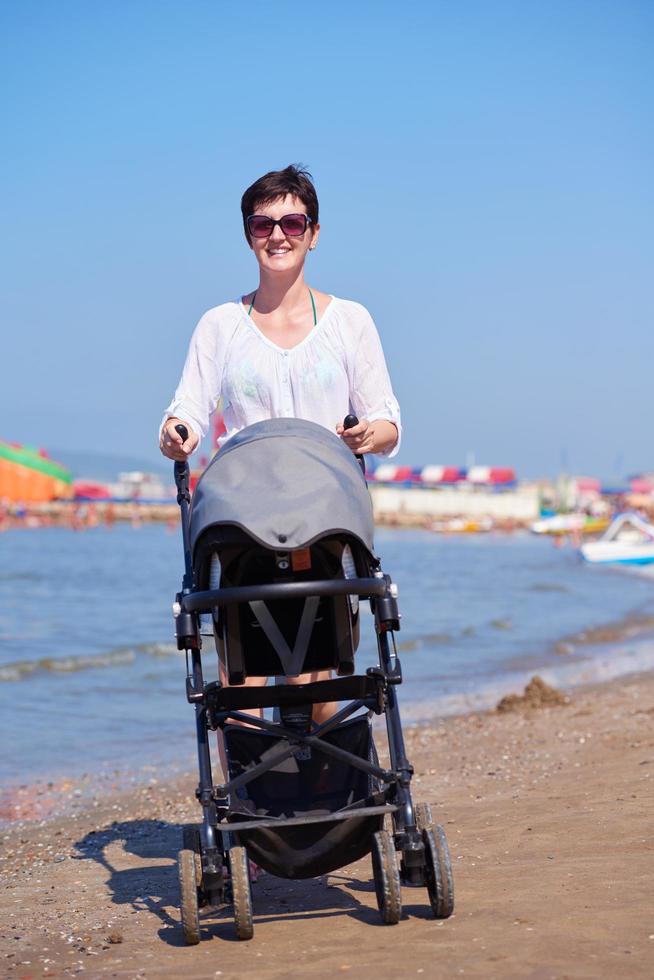 madre a piedi su spiaggia e spingere bambino carrozza foto