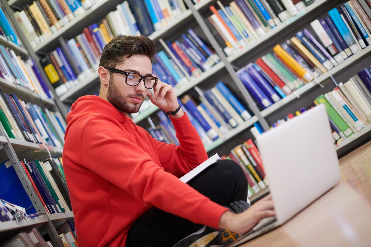 il studenti usi un' taccuino, il computer portatile e un' scuola biblioteca foto