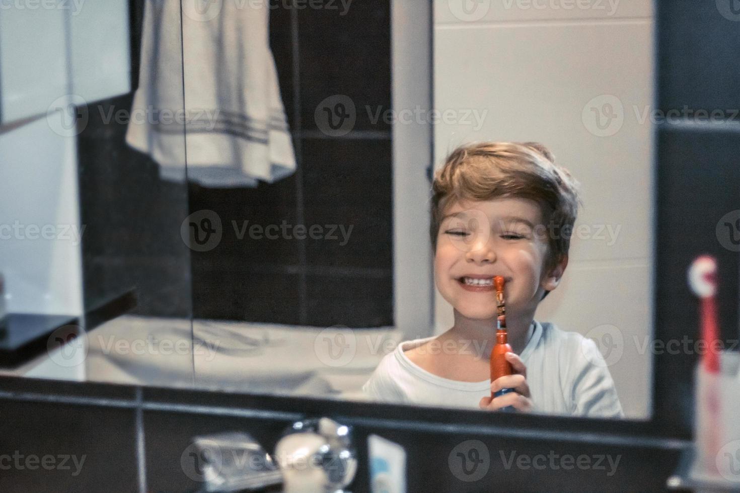 poco ragazzo spazzolatura denti nel il mattina. foto