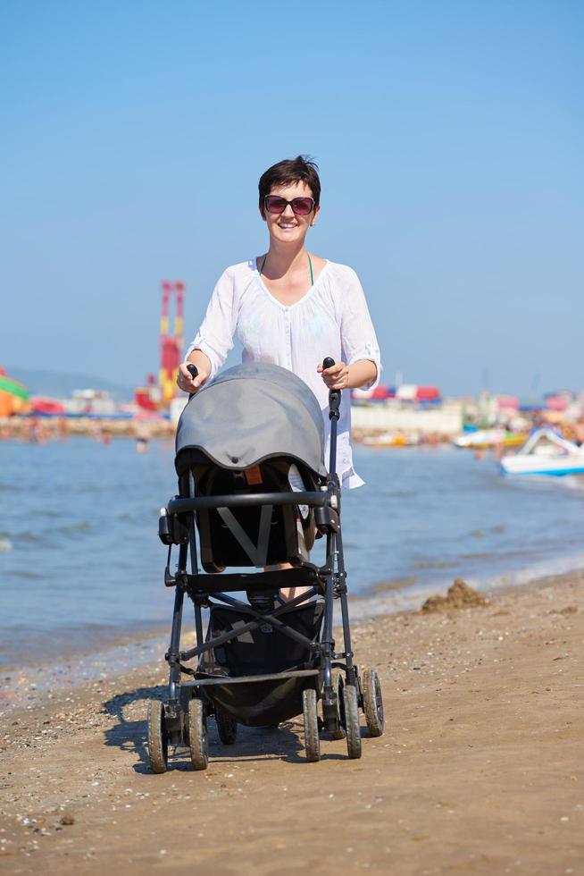 madre a piedi su spiaggia e spingere bambino carrozza foto