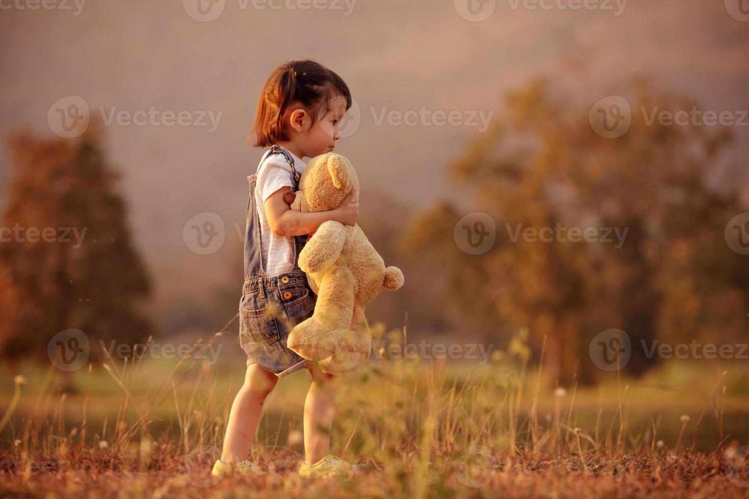 poco carino ragazza in piedi nel il erba Tenere grande orsacchiotto orso, retrò filtro effetto foto