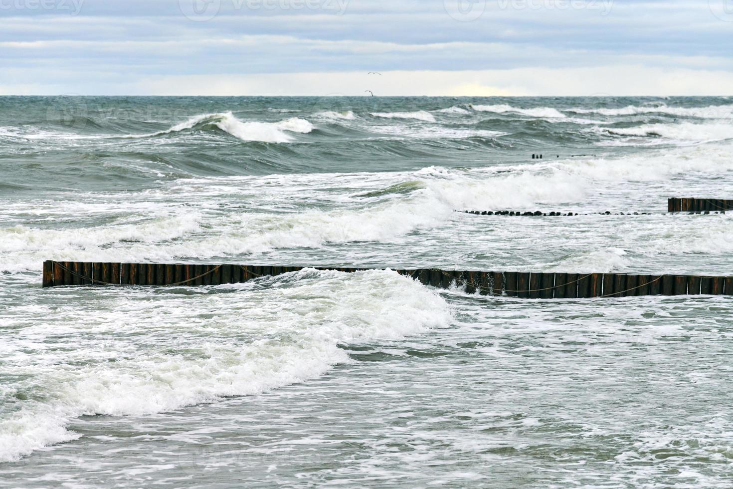 vista del mare blu con onde spumeggianti e frangiflutti in legno foto