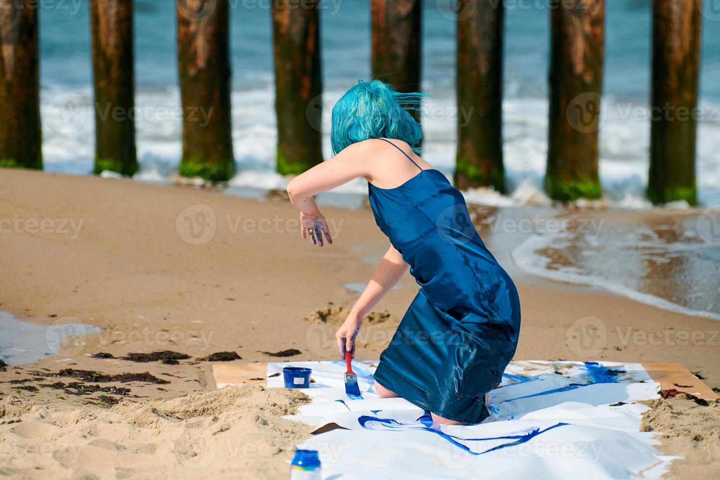 artista di performance artistica donna dai capelli blu imbrattata con pitture a guazzo su grande tela sulla spiaggia foto