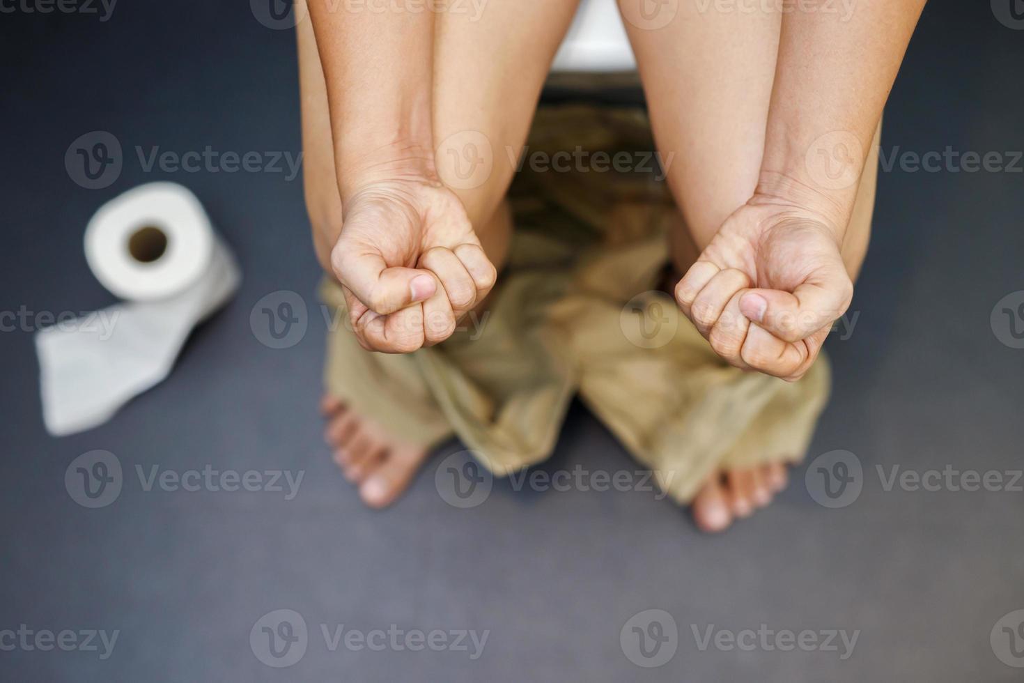 uomo soffre a partire dal diarrea mano hold fazzoletto di carta carta rotolo nel davanti di gabinetto ciotola. stipsi nel bagno. trattamento stomaco dolore e igiene, Salute cura foto