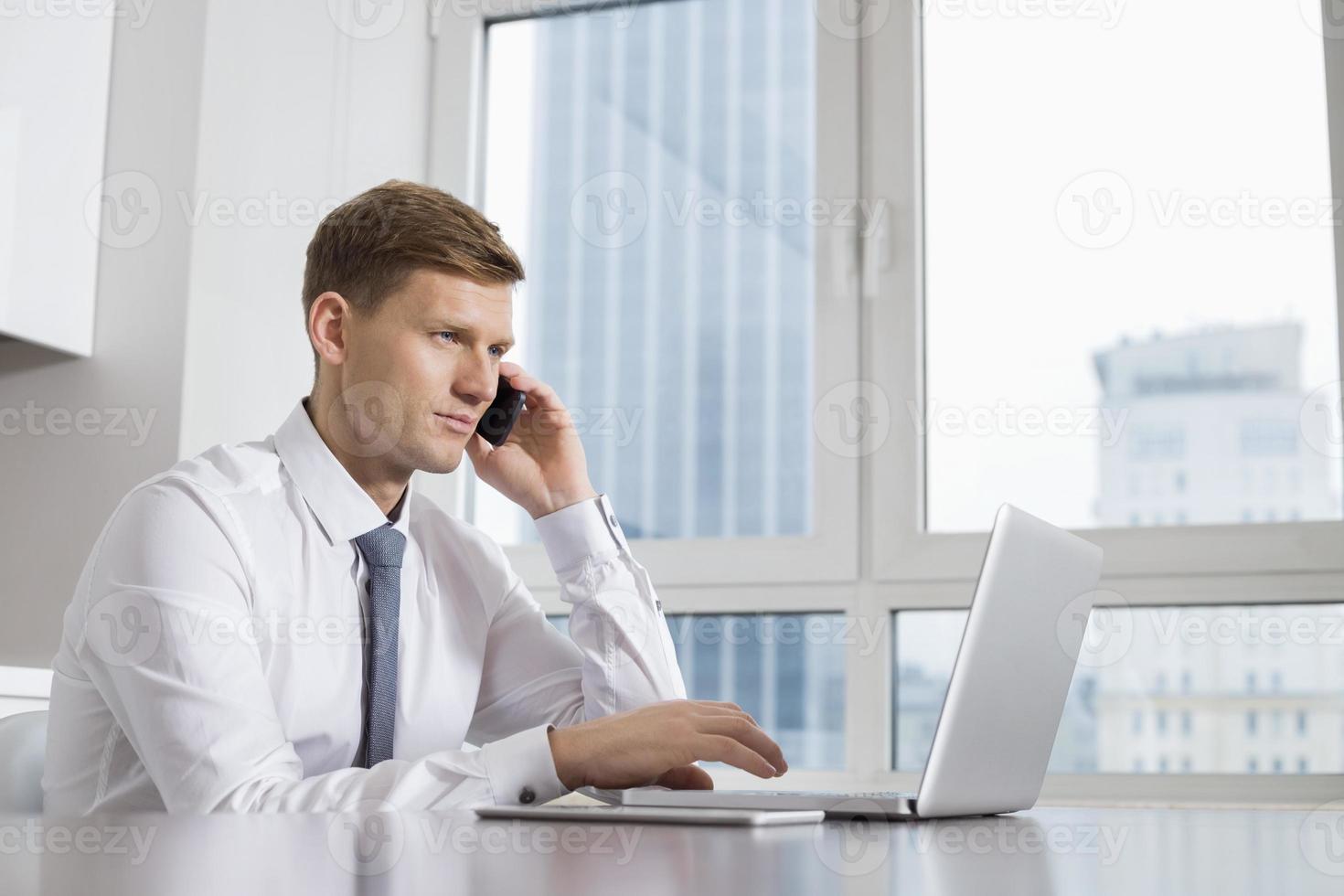 metà uomo d'affari adulto su chiamata mentre si utilizza il laptop a casa foto