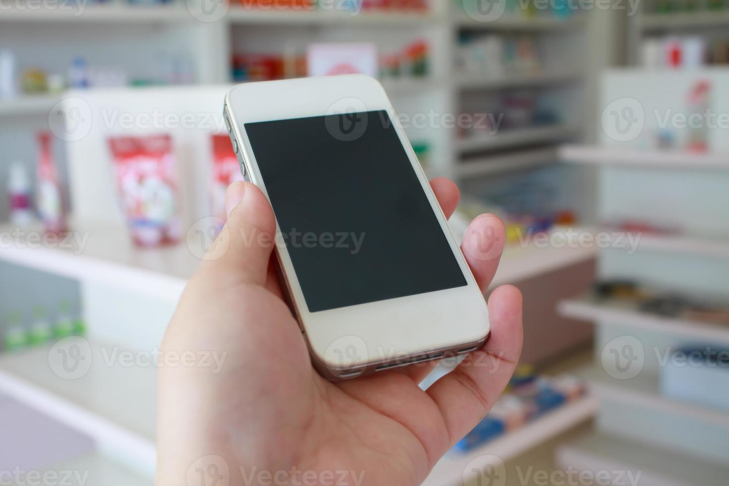 mano che tiene smartphone con sfocatura alcuni scaffali di droga nella farmacia farmacia foto