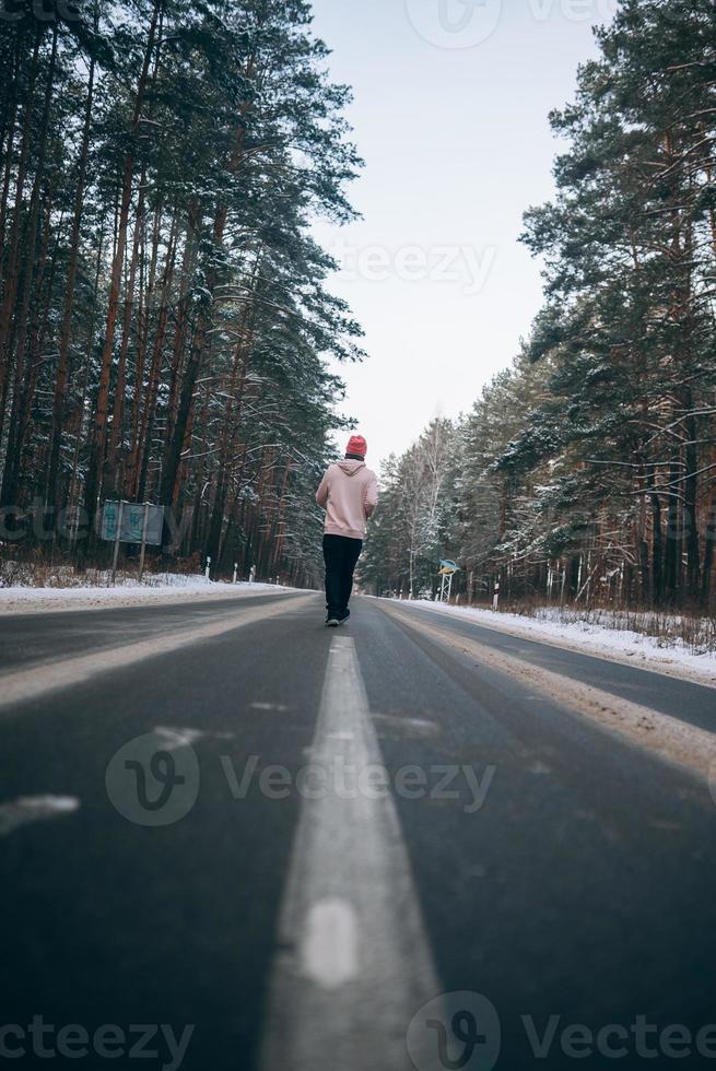 tipo in piedi su il strada nel il mezzo di il foresta, circondato di neve foto