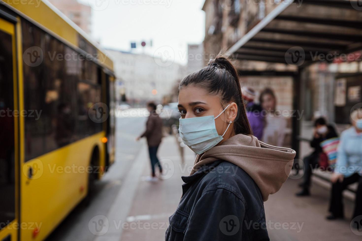 giovane donna indossare chirurgico maschera all'aperto a autobus fermare nel il strada foto