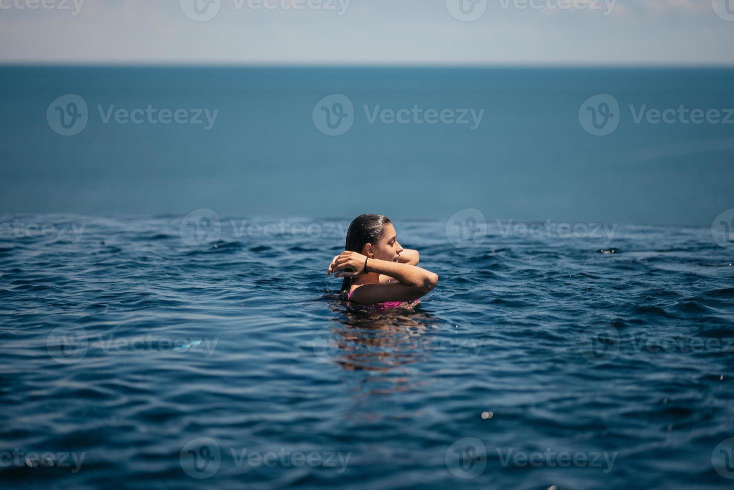 contento donna nel costume da bagno nuoto nel infinito piscina contro lungomare. foto