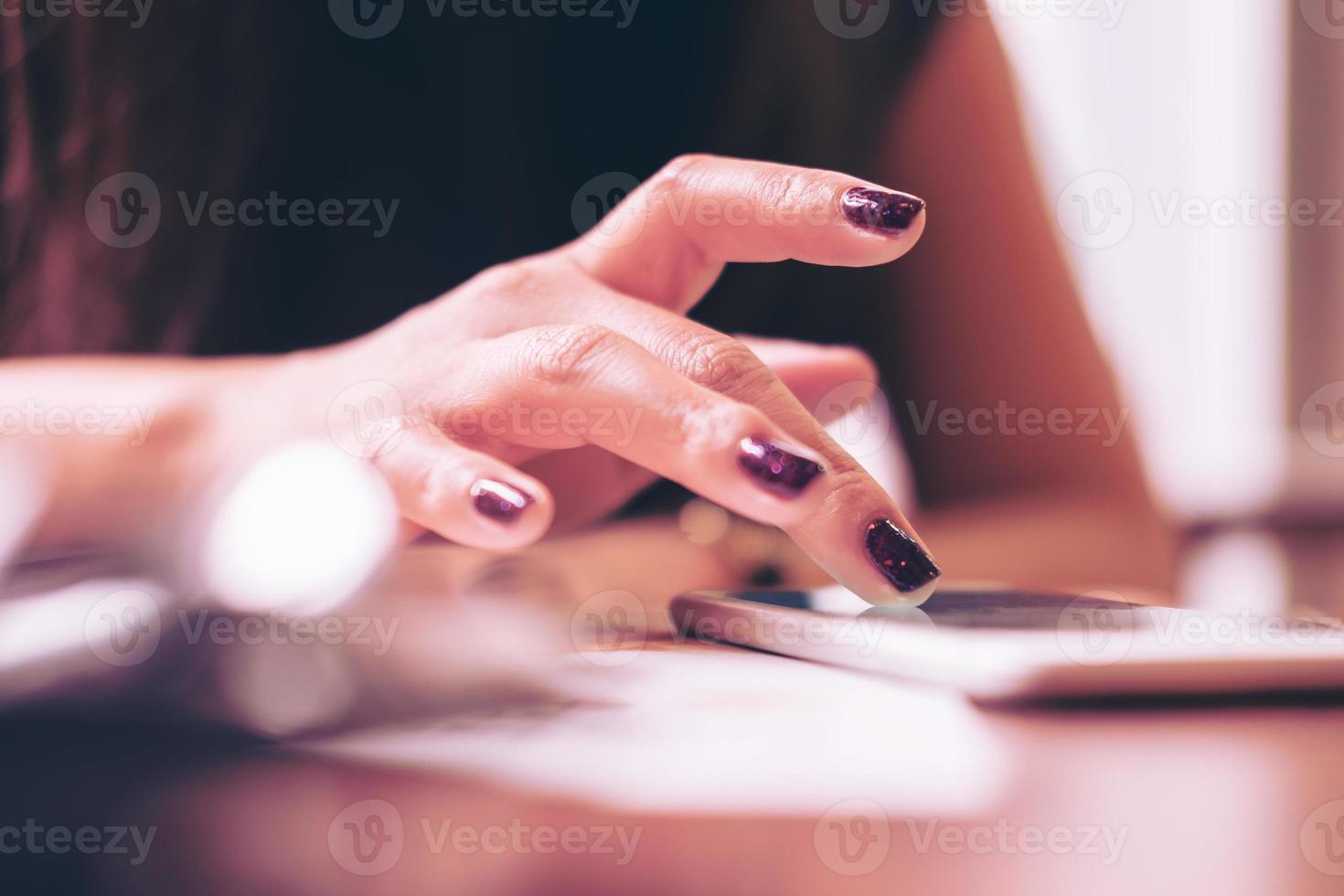 le mani di una donna d'affari toccando lo schermo del telefono intelligente sul tavolo di legno nella moderna caffetteria foto