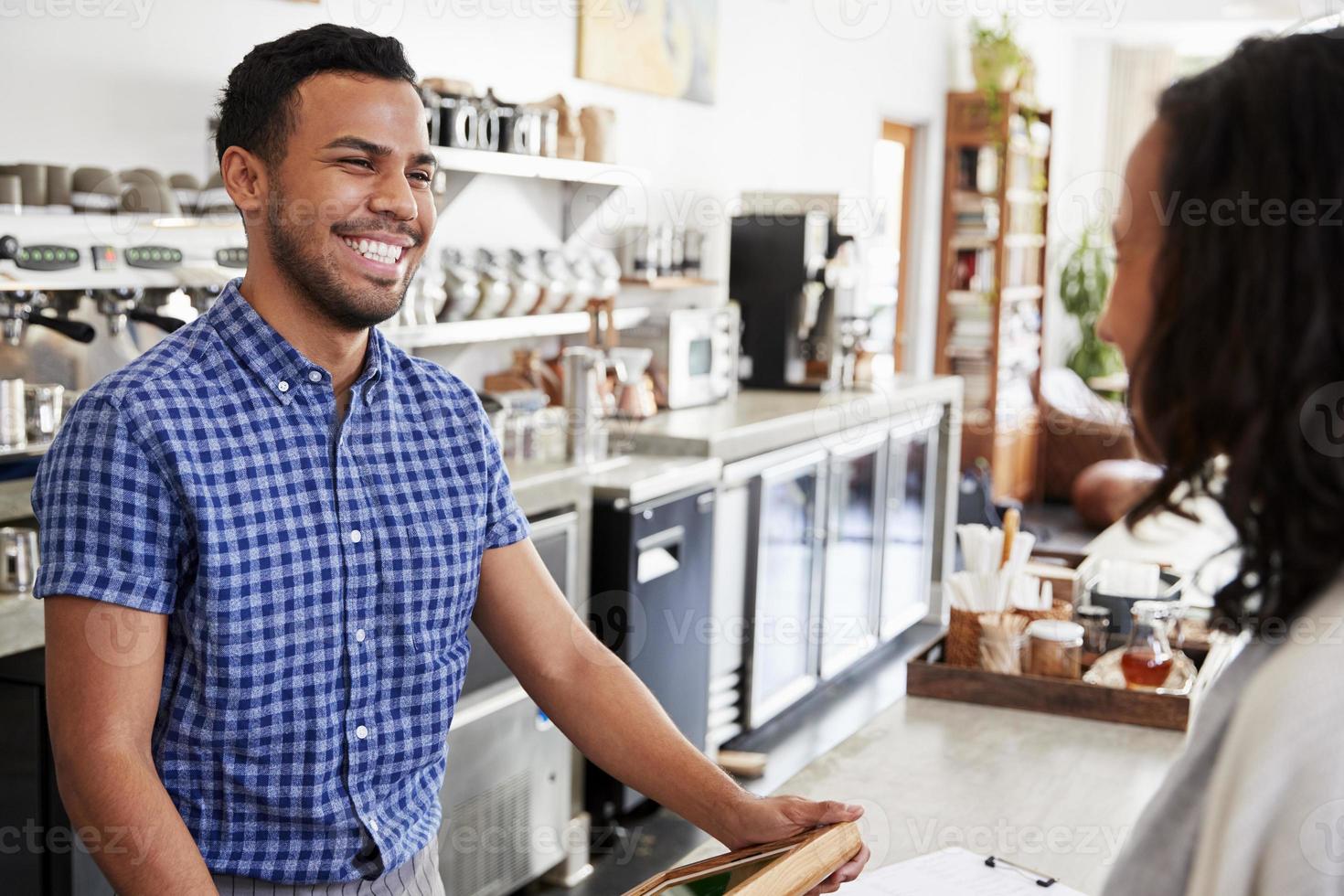 il barista maschio sorride ad un cliente femminile in una caffetteria foto
