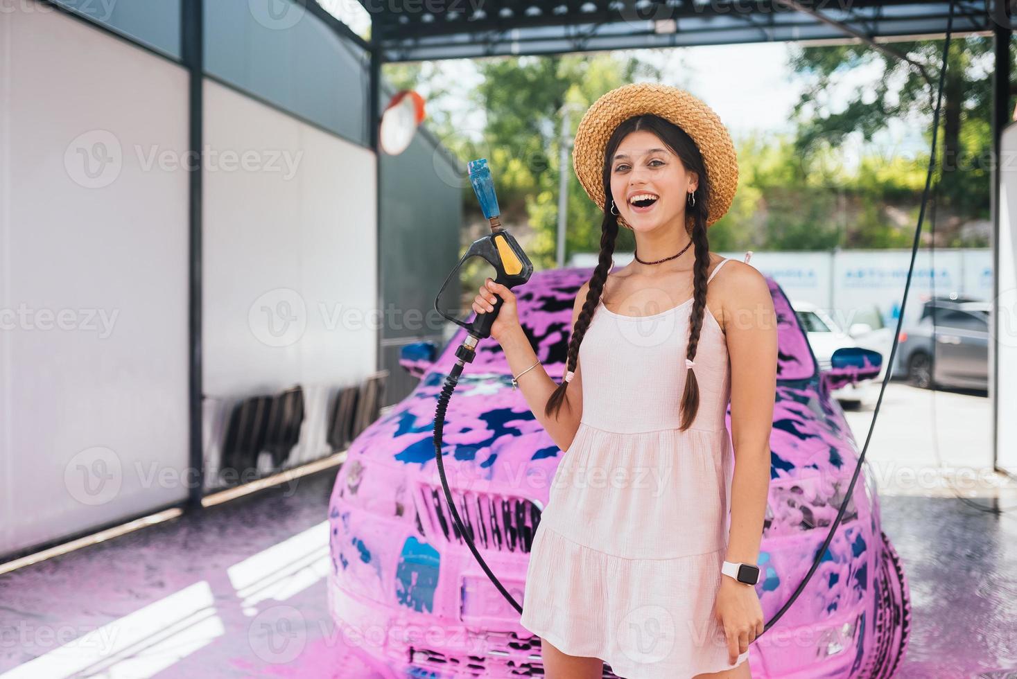 giovane donna tubo flessibile sta nel davanti di un' auto coperto nel rosa schiuma foto