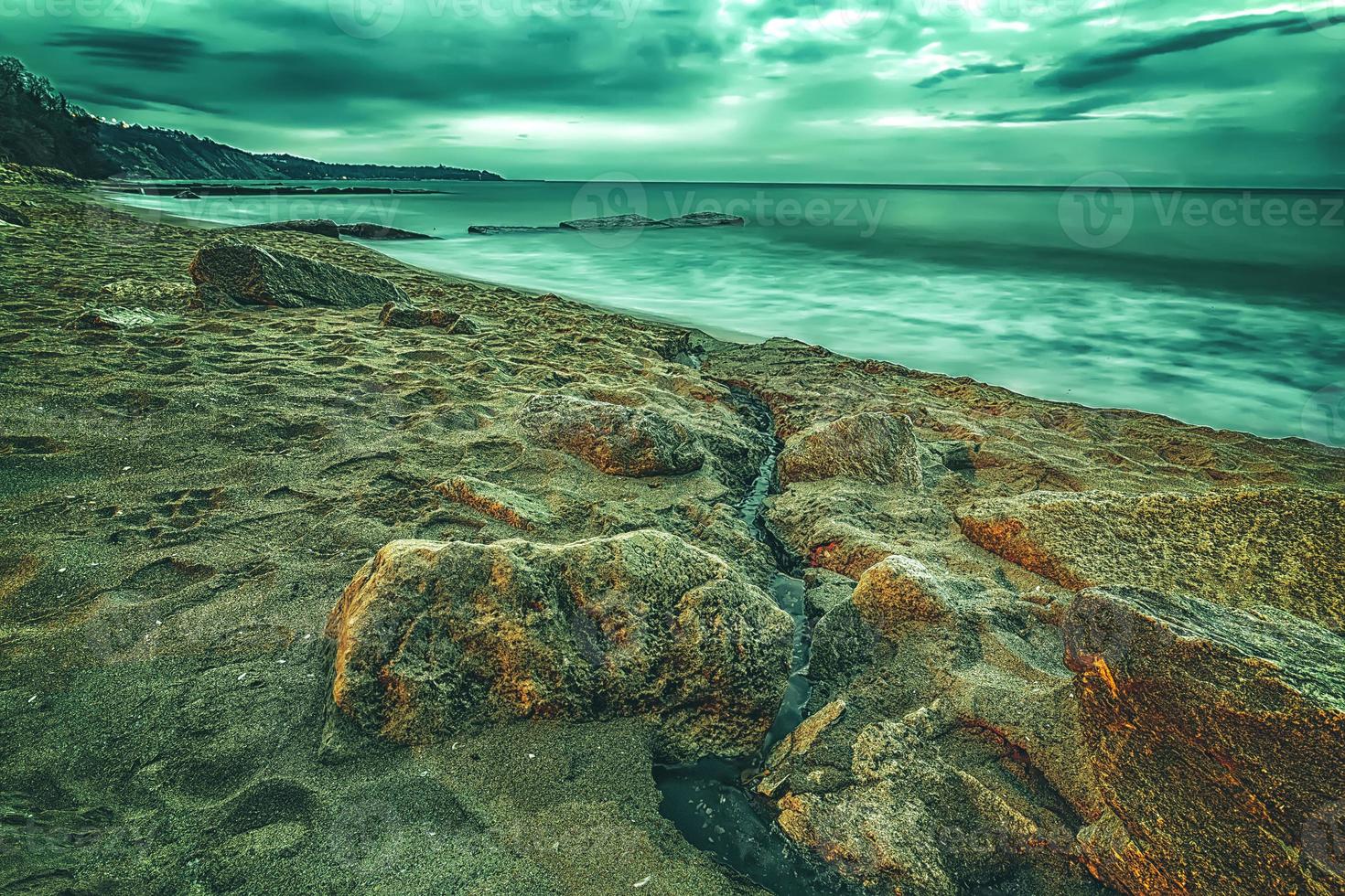 creativo Visualizza di nuvoloso Alba con movimento sfocatura mare e rocce su il spiaggia foto