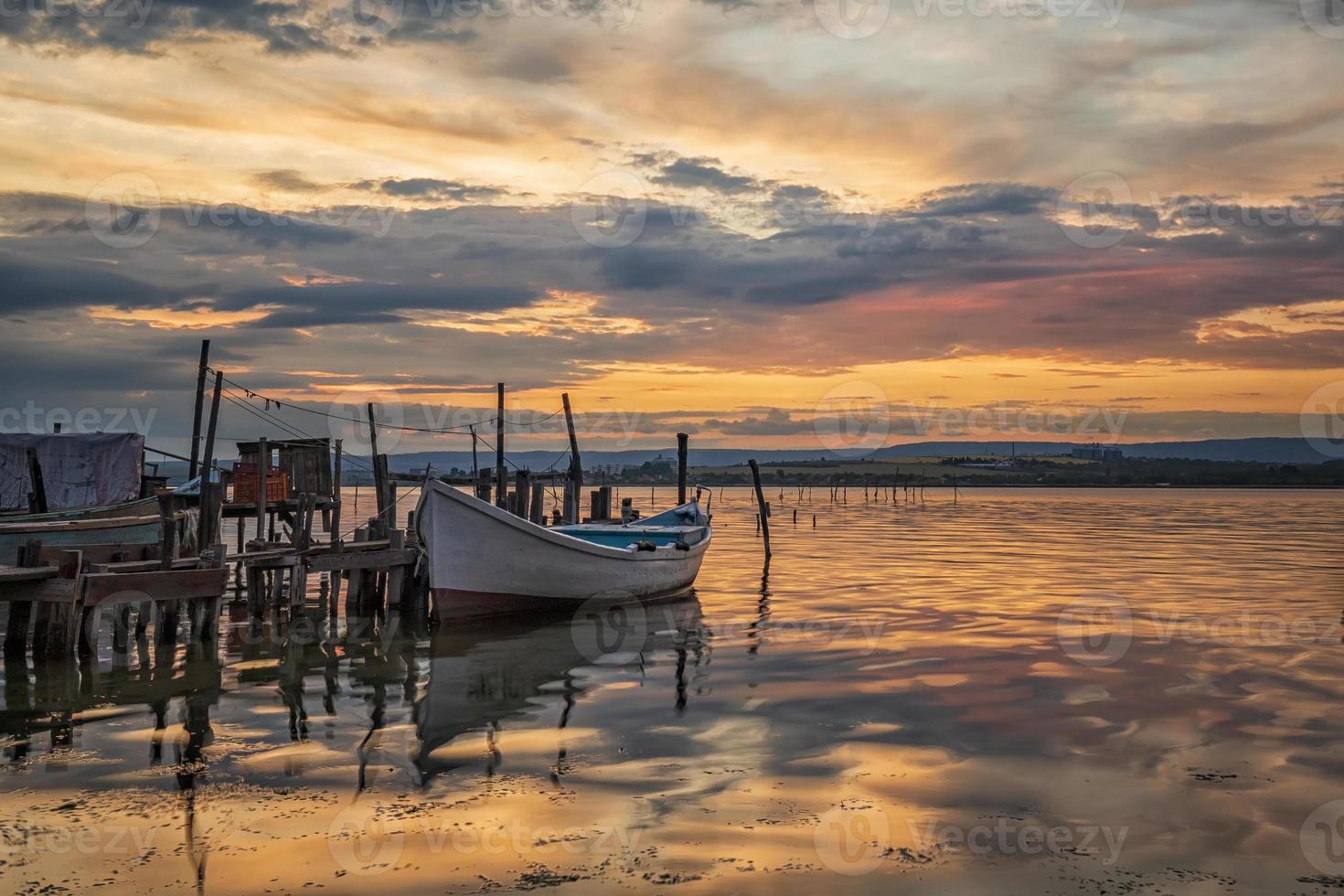 sorprendente colorato tramonto a un' lago con un' barca a un' di legno molo. orizzontale Visualizza foto