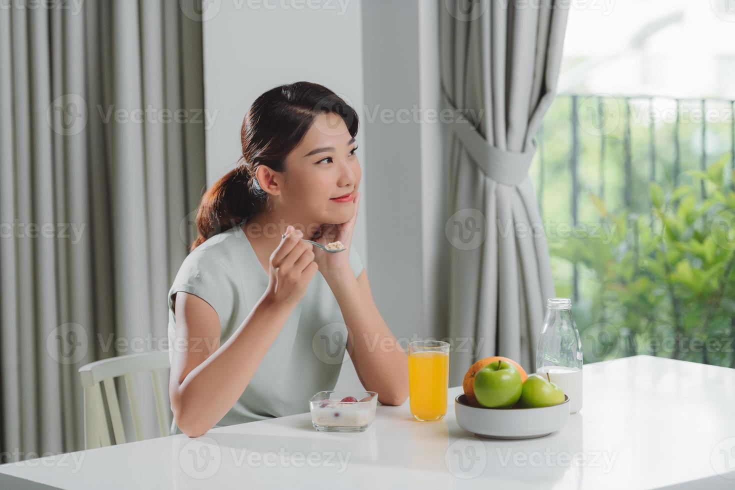 riflessivo giovane donna nel accappatoio mangiare prima colazione nel cucina foto