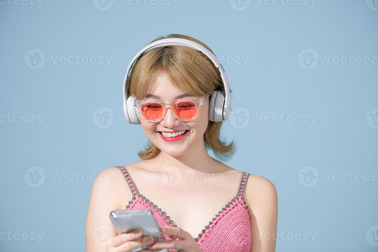 ottimista positivo asiatico ragazza gode ogni po di musica indossa stereo cuffie su sua orecchie detiene un' mobile Telefono ascolta per preferito Audio traccia foto