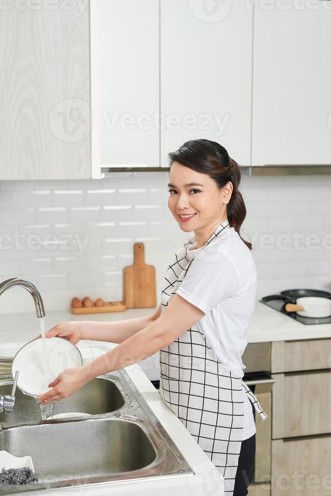 bellissimo sorridente giovane donna lavaggio il piatti nel moderno bianca cucina. foto