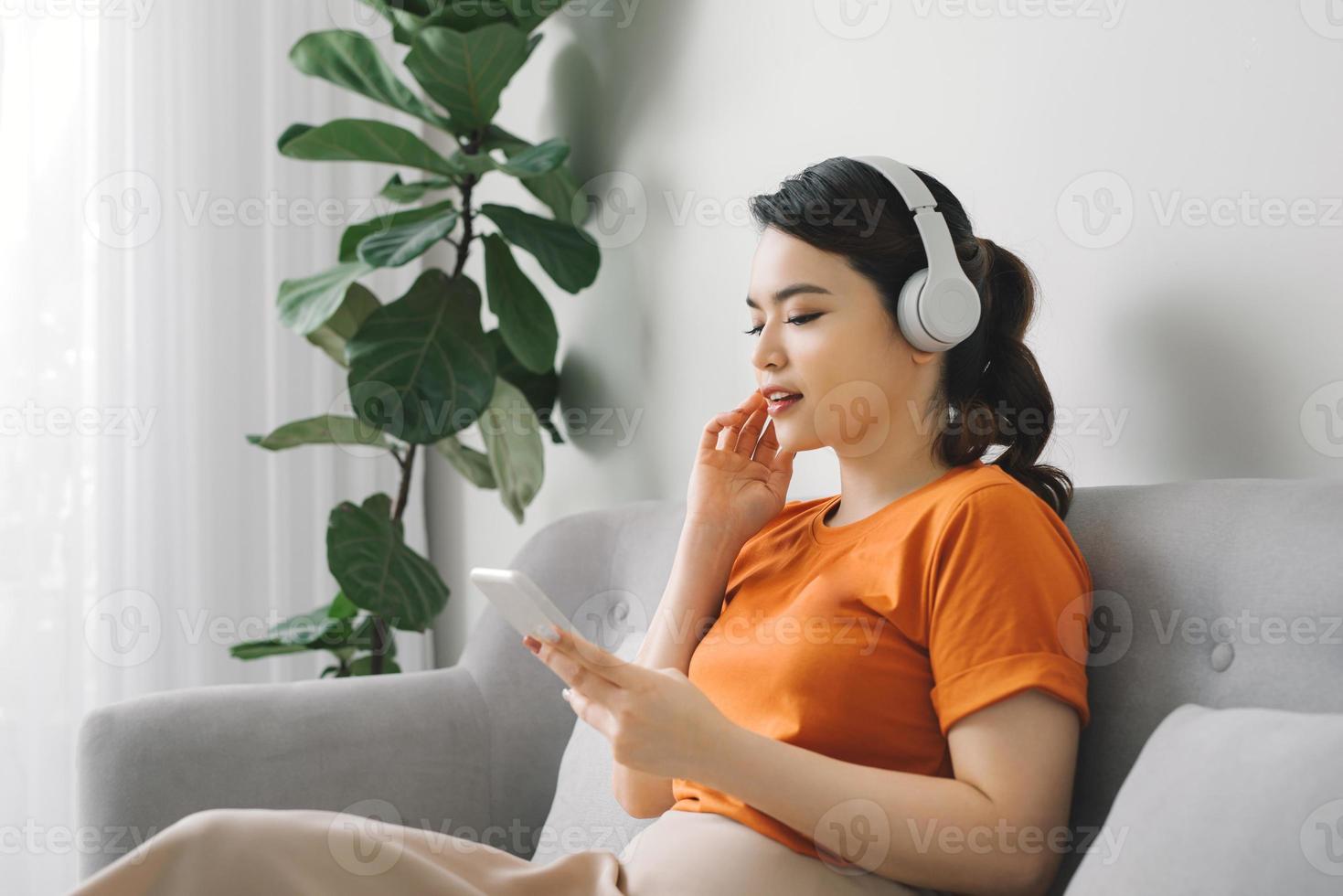 ritratto di un' allegro giovane donna ascoltando per musica con mobile Telefono mentre riposo su un' divano a casa foto