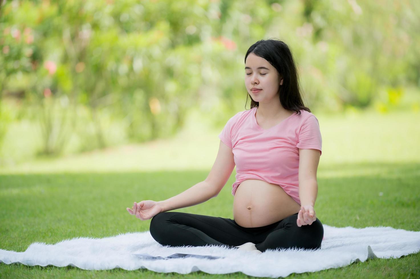 un' incinta asiatico donna rilassa con yoga allungamento esercizi nel il parco per il Salute di il madre e il nascituro bambino foto