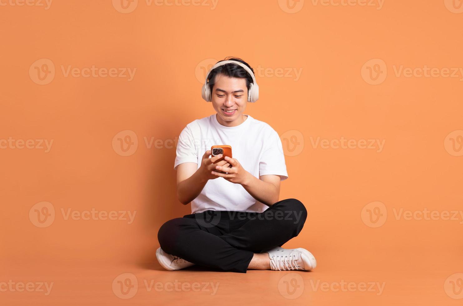 Immagine di asiatico uomo seduta utilizzando Telefono e isolato su arancia sfondo foto