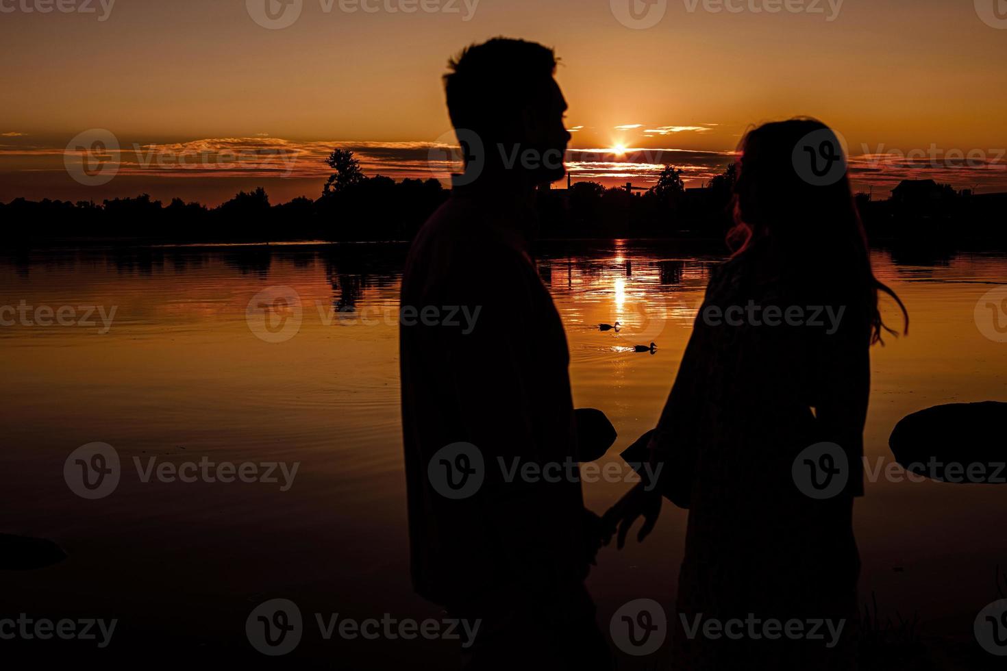 silhouette di amorevole coppia abbracciare su il lago a tramonto. bellissimo giovane coppia nel amore a piedi su il riva di il lago a tramonto nel il raggi di luminosa luce. copia spazio. selettivo messa a fuoco. foto
