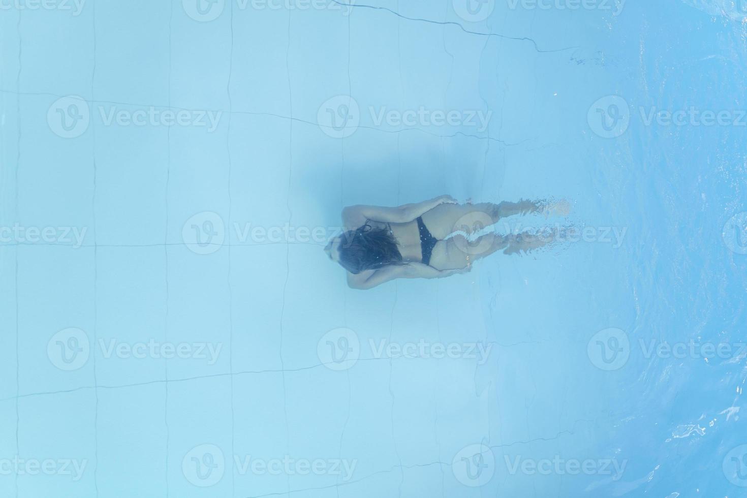 attraente giovane donna galleggiante nel un' nuoto piscina con sua braccia disteso, guardare a il cielo foto