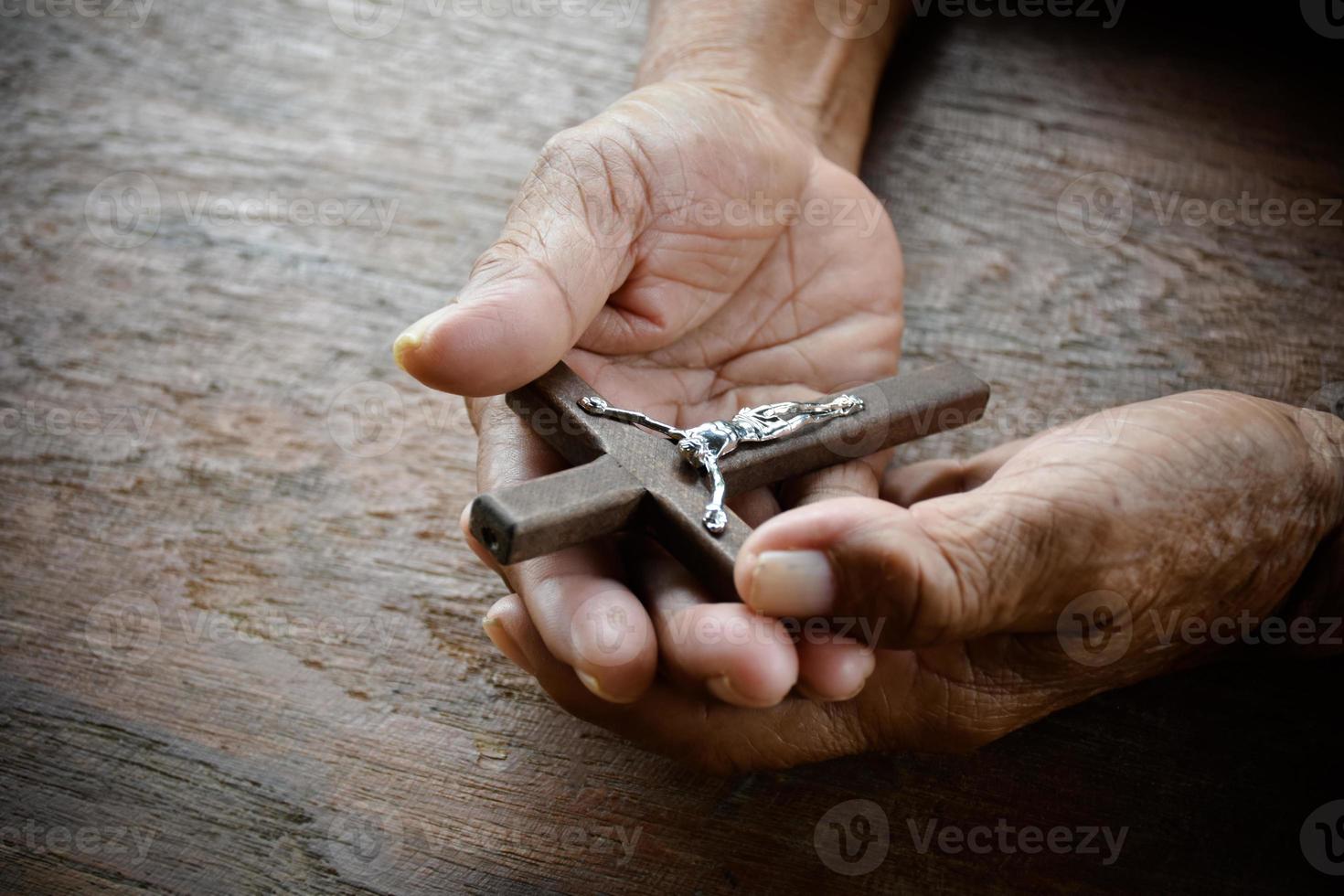 avvicinamento di legno attraversare quale ha un' metallo statua di crocifisso Gesù è nel il mani di un asiatico anziano cattolico mentre preghiere nel un' Locale Chiesa, morbido e selettivo messa a fuoco. foto