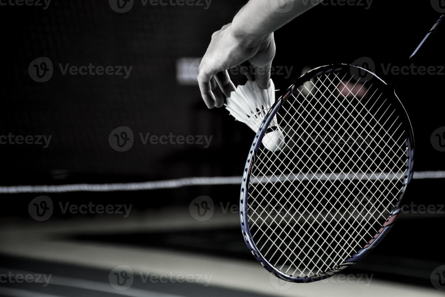 badminton giocatore detiene racchetta e bianca crema volano nel davanti di il netto prima servendo esso per un altro lato di il Tribunale. foto