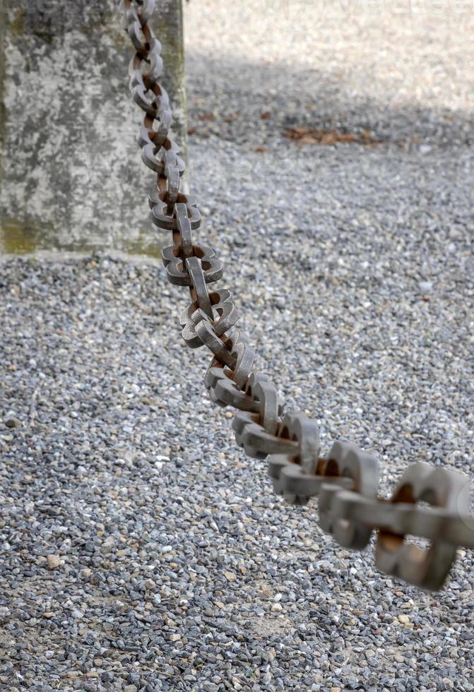 un' leggero grigio metallo catena fatto di acciaio e mostrando suo età è visto su vicino come esso si blocca sopra il rotto pietra zavorra. selettivo messa a fuoco. foto