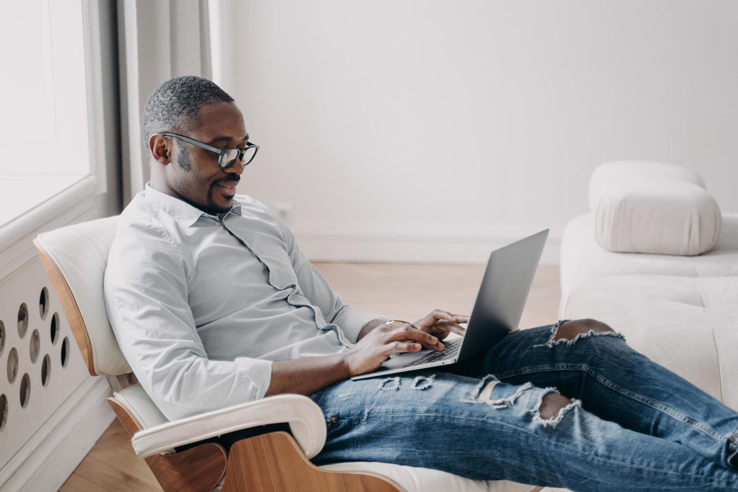 focalizzata africano americano uomo d'affari Lavorando digitando su il computer portatile seduta nel sedia a casa ufficio foto